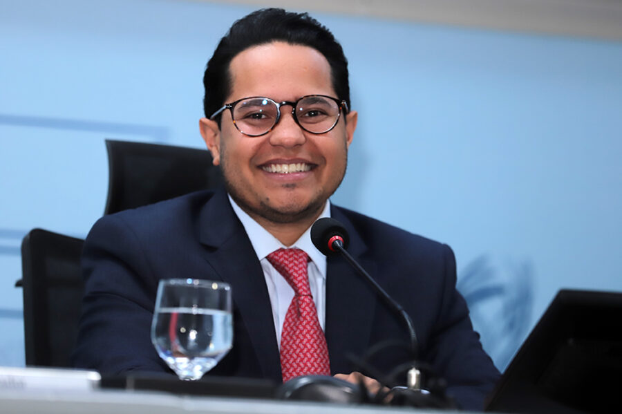 Vereador Papy em um evento público, com fundo institucional e bandeiras ao fundo.