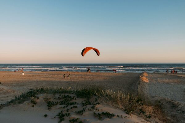 Man paragliding over Arroio do Silva beach during sunset, showcasing vibrant recreation.