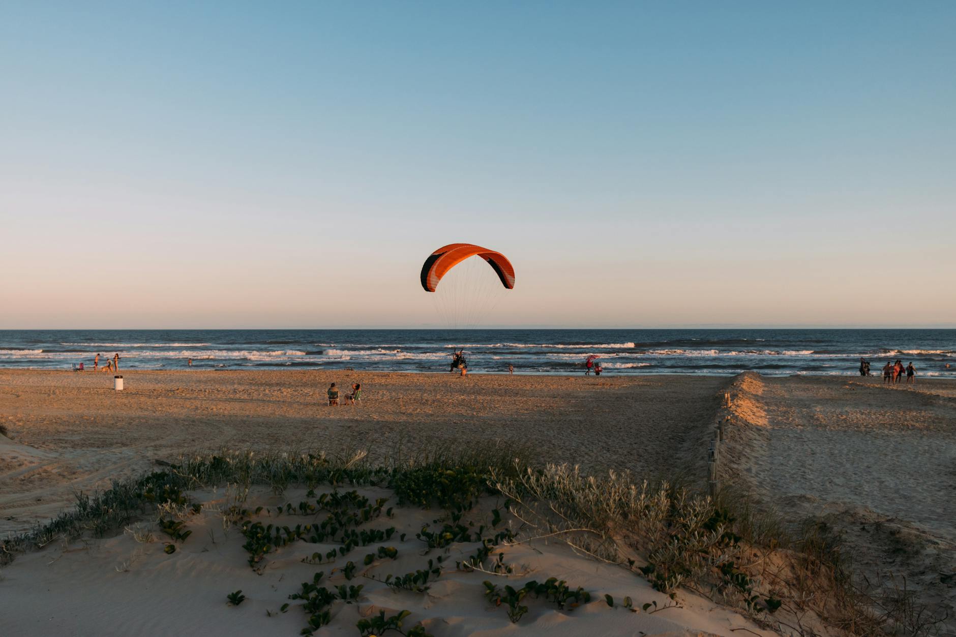 Man paragliding over Arroio do Silva beach during sunset, showcasing vibrant recreation.