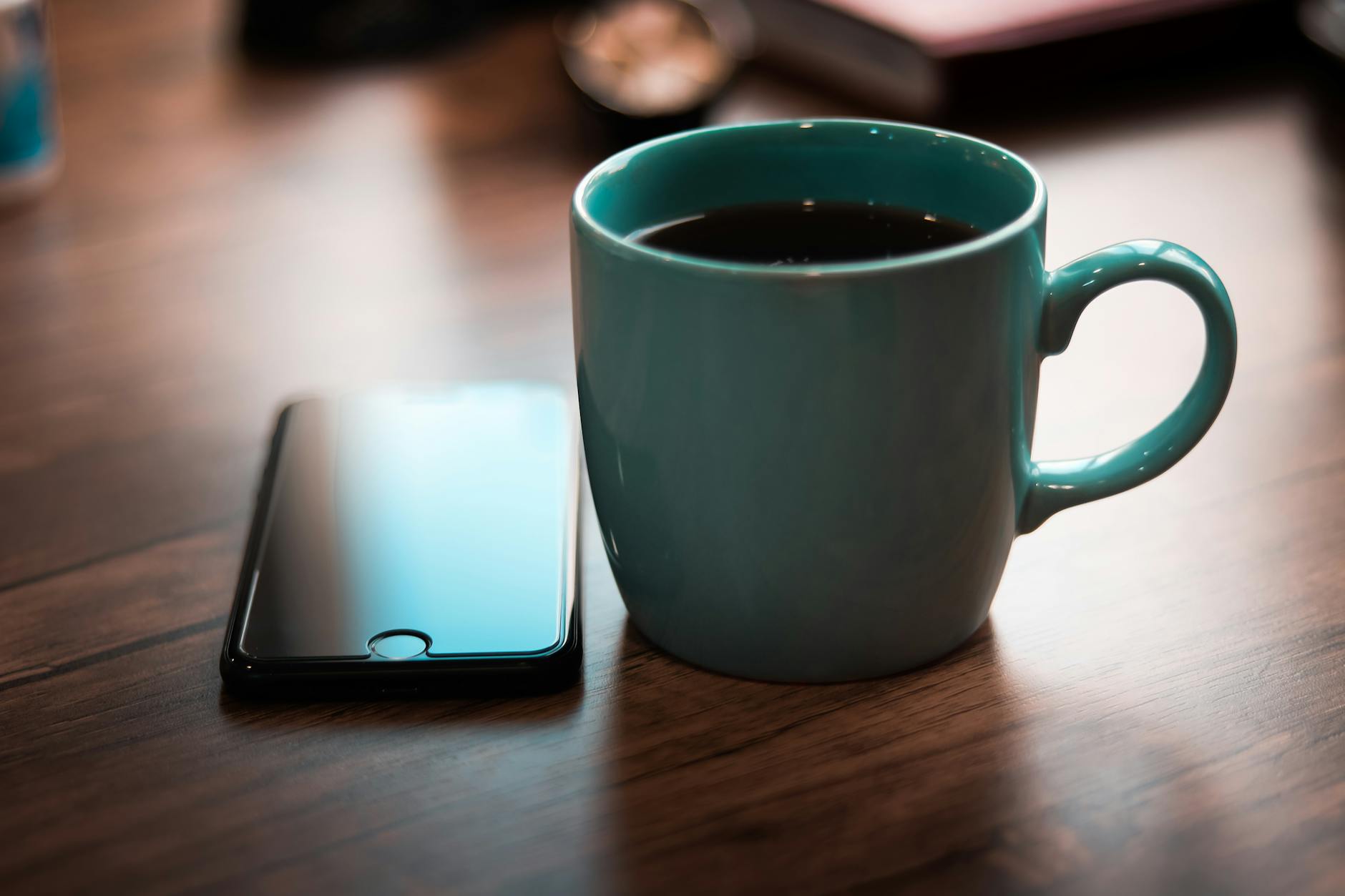 A coffee mug and smartphone on a wooden table, capturing a cozy and modern atmosphere.