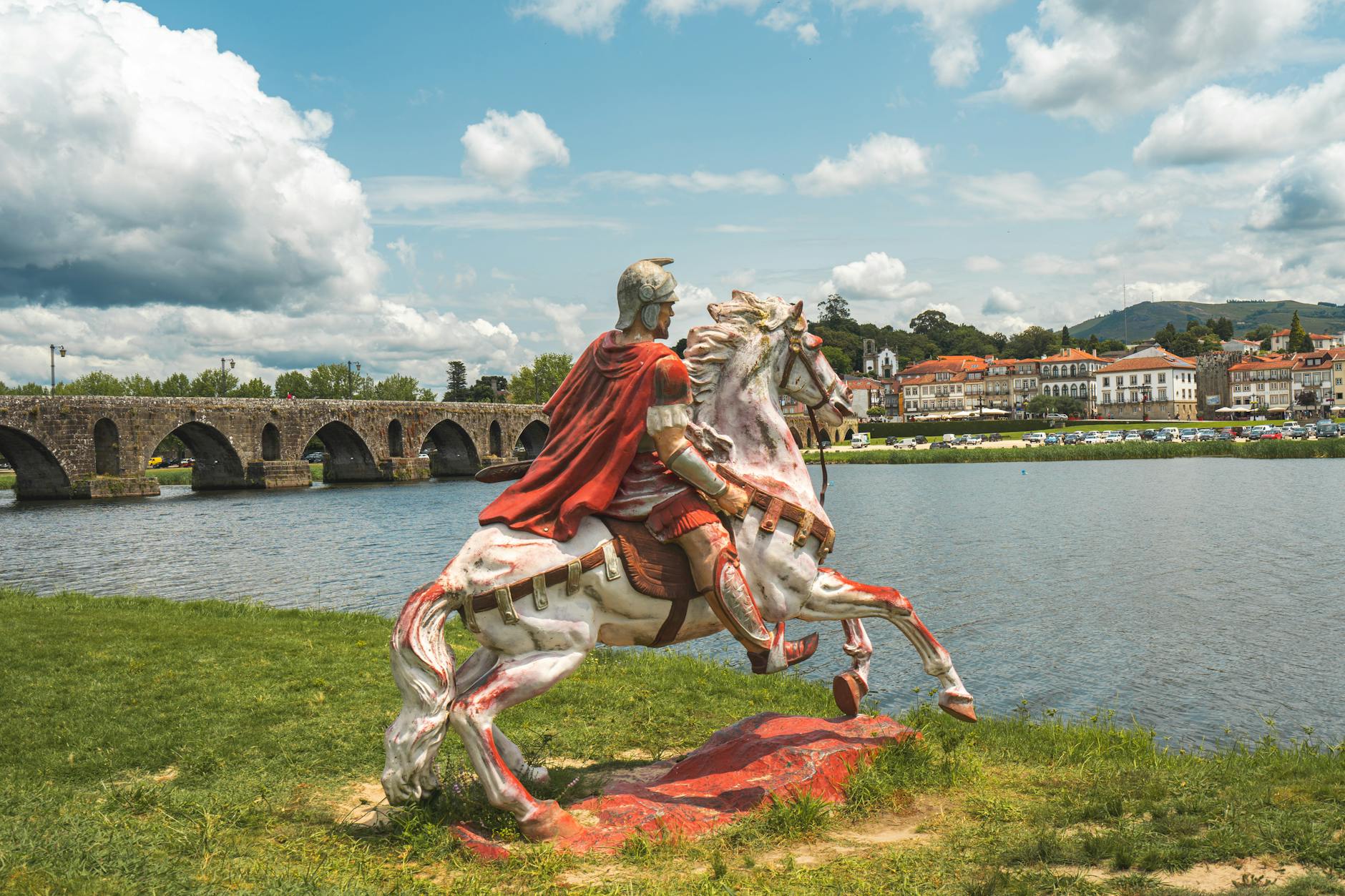 A striking statue of Roman cavalry with a scenic backdrop of Ponte de Lima and its iconic bridge in Portugal.