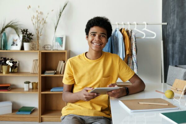 Senado Aprova Lei de Combate à Desinformação Online Smiling teenager using a tablet at his desk for online learning at home.