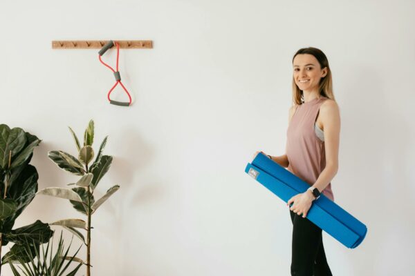 CNJ Expande Programa de Justiça Restaurativa em Presídios Smiling woman holding a blue yoga mat, preparing for a fitness session at home, emphasizing a healthy lifestyle.