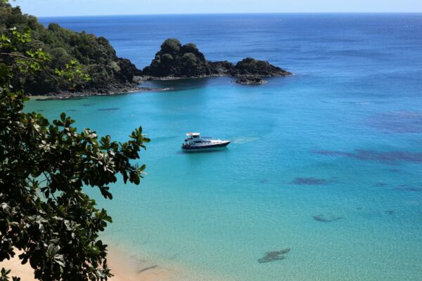 Criptomoedas: Esquema Ponzi Bilionário Desmantelado no Brasil A breathtaking aerial view of a clear turquoise bay in Brazil with a boat and lush cliffs.
