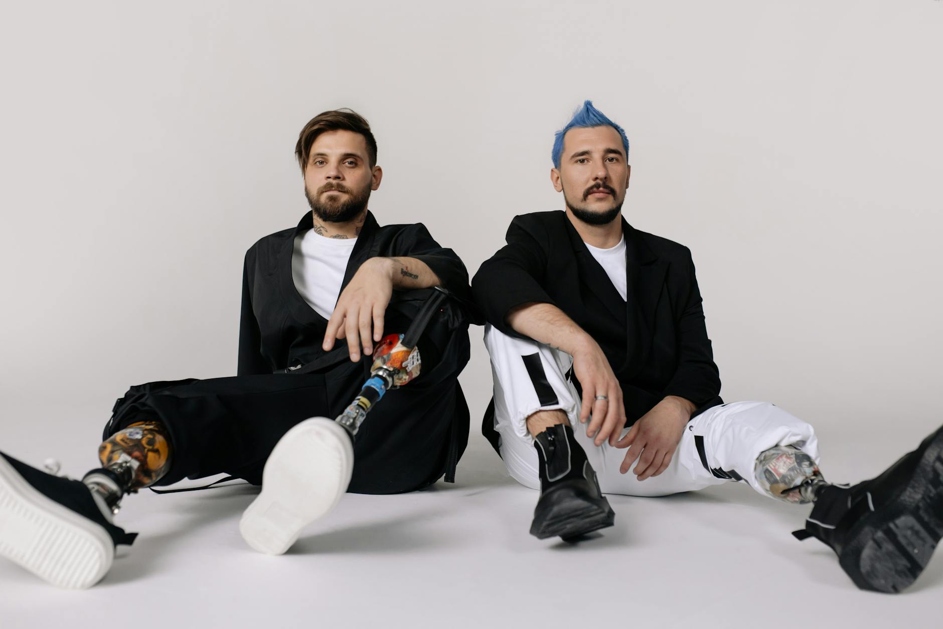 Two stylish men with prosthetic legs sitting in a studio, embodying modern fashion and empowerment.