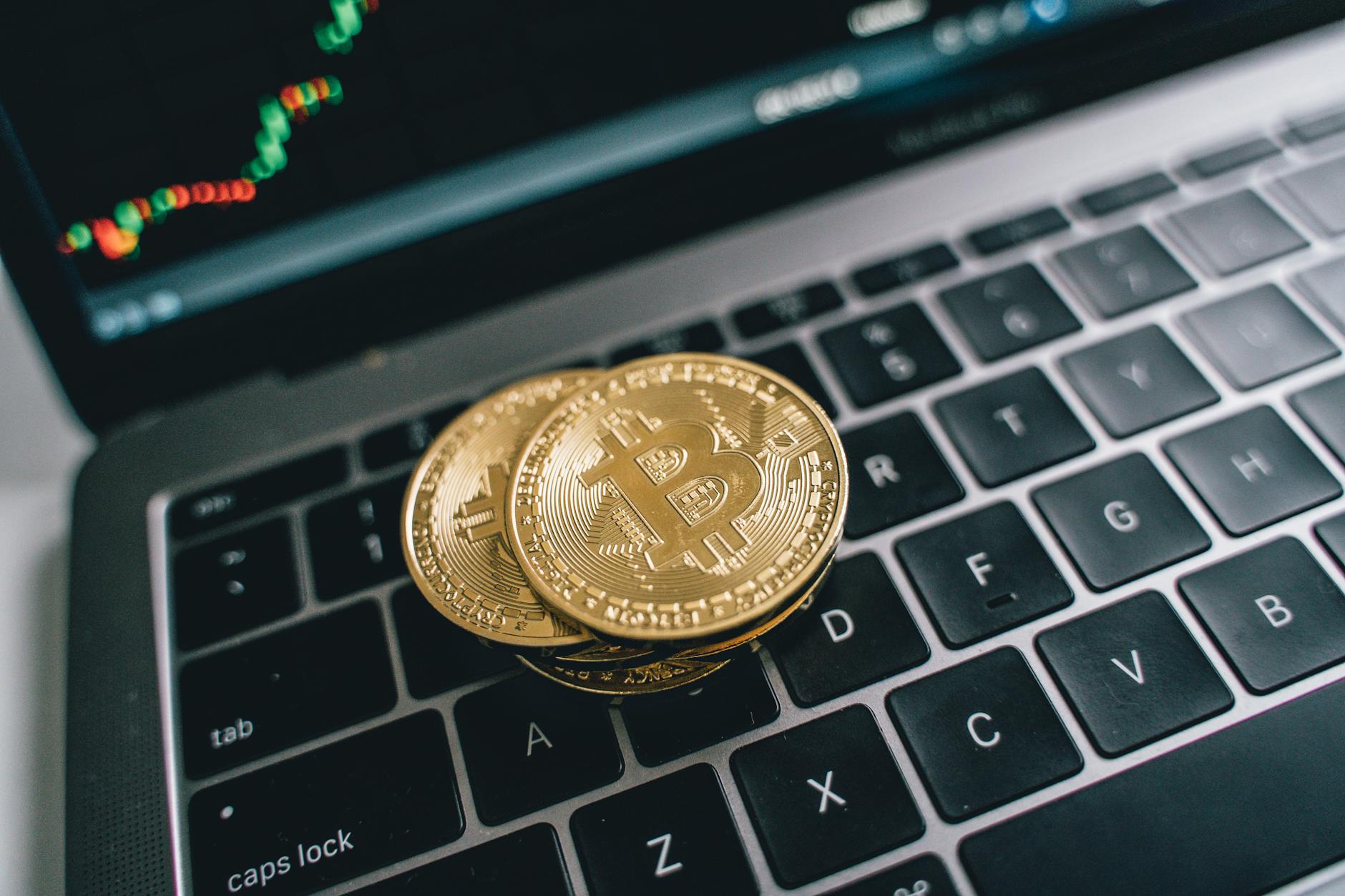 Close-up of golden bitcoins on a laptop keyboard depicting cryptocurrency and trade concepts with a market chart in the background.