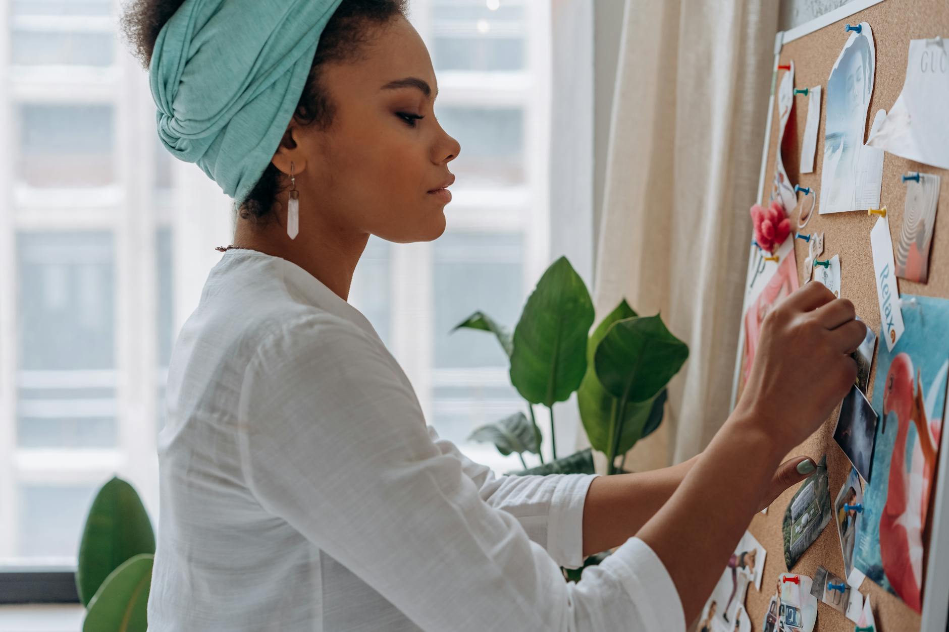 A woman in a headwrap adding photos to a corkboard, promoting focus and creativity.