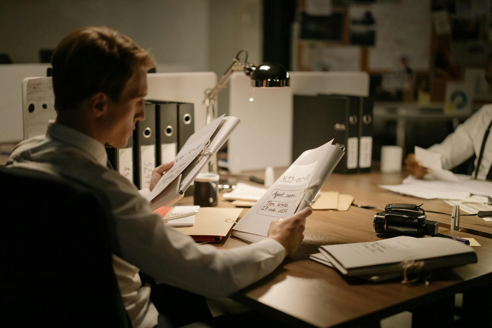 Two detectives reviewing documents in a dimly lit office setting, focused and professional.