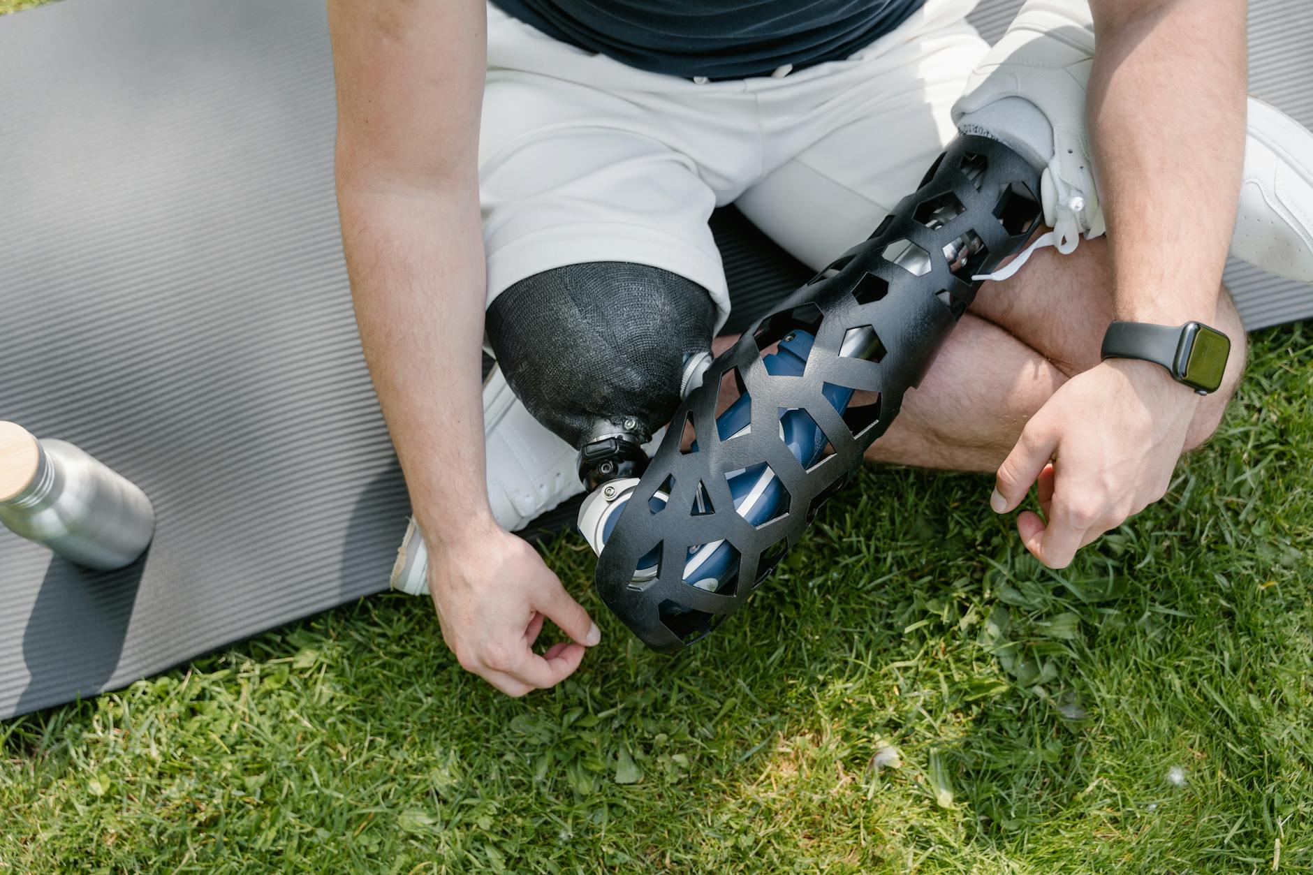 Close-up of a person with a prosthetic leg sitting on grass with exercise mat, embracing a healthy lifestyle.