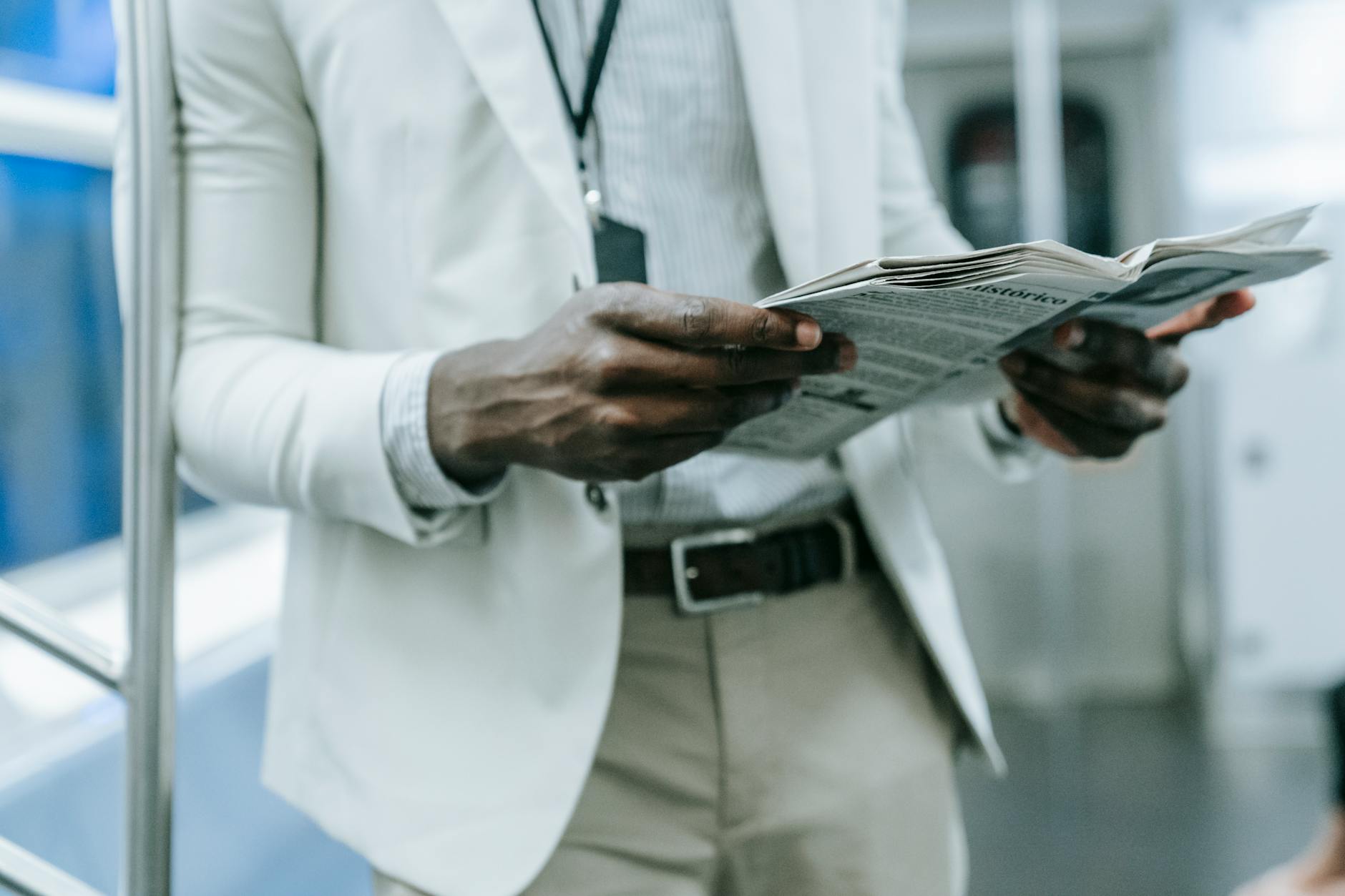 A professional in a blazer reads a newspaper while commuting on a train.
