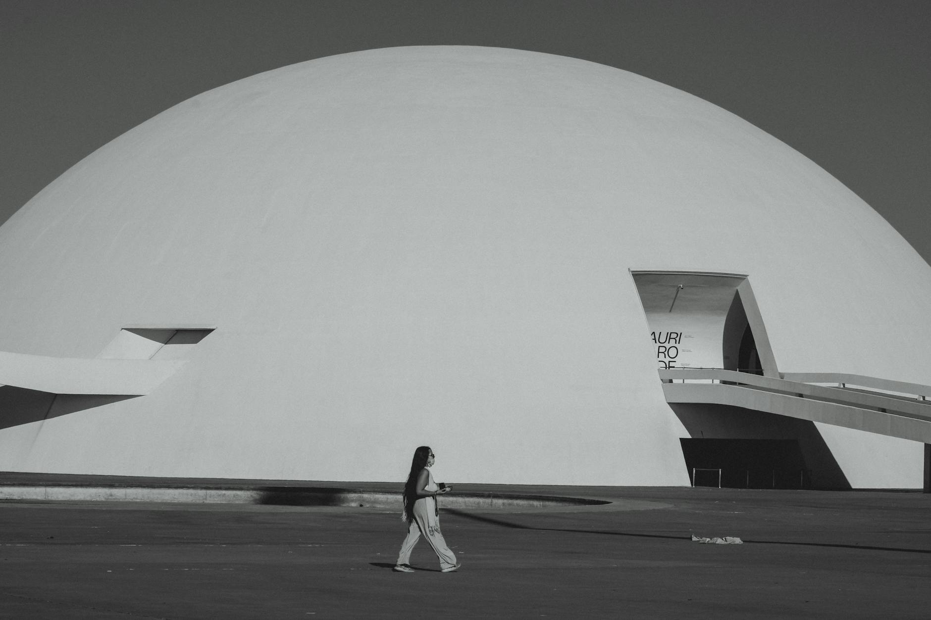 A woman walks by the futuristic Niemeyer Dome in Brasília, showcasing modern architecture.