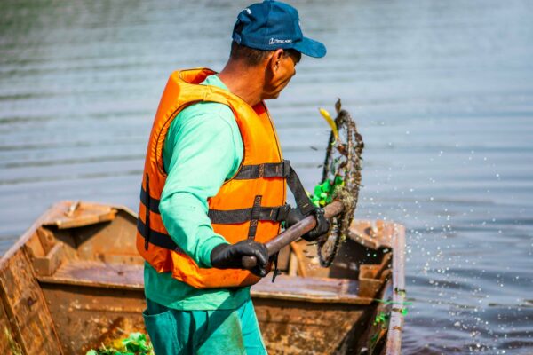 Cresce a Busca por Refúgio Climático no Sul do Brasil A worker cleaning a lake in Londrina, Brasil, wearing a life vest and using a net.