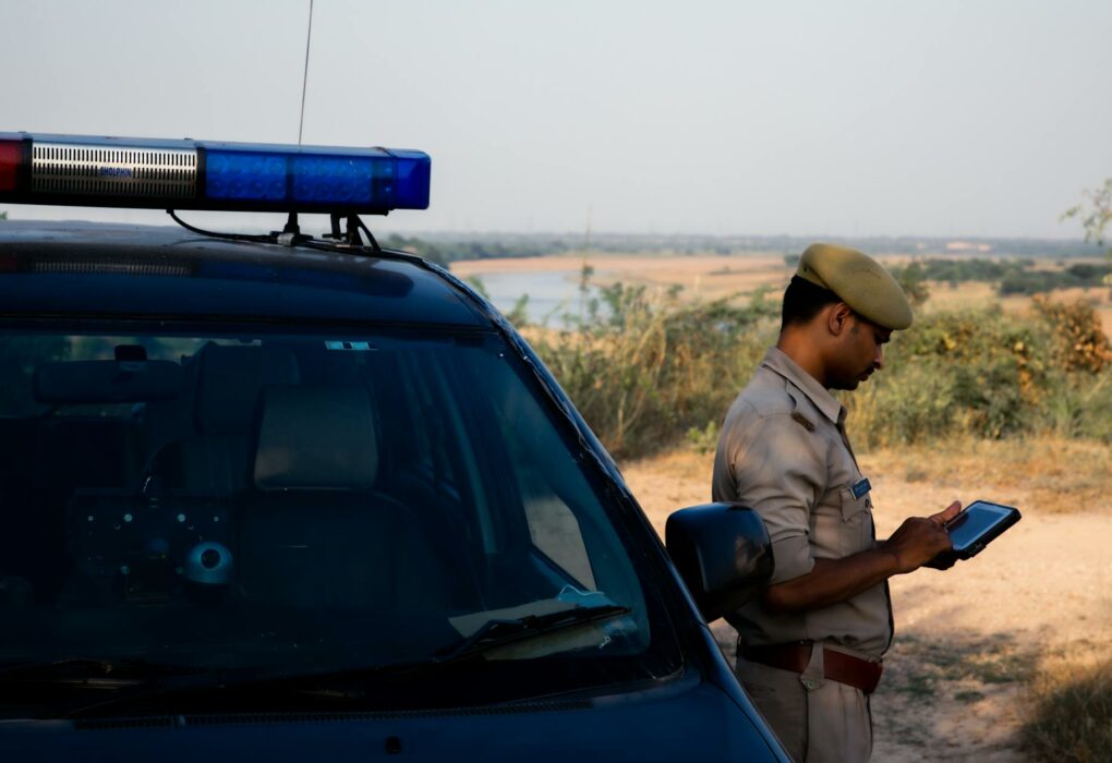 STJ Cimenta Requisitos Essenciais para Validade da Prova Digital A police officer using a tablet beside a patrol car in a rural outdoor setting.