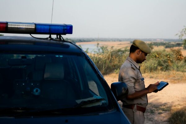 STJ Cimenta Requisitos Essenciais para Validade da Prova Digital A police officer using a tablet beside a patrol car in a rural outdoor setting.