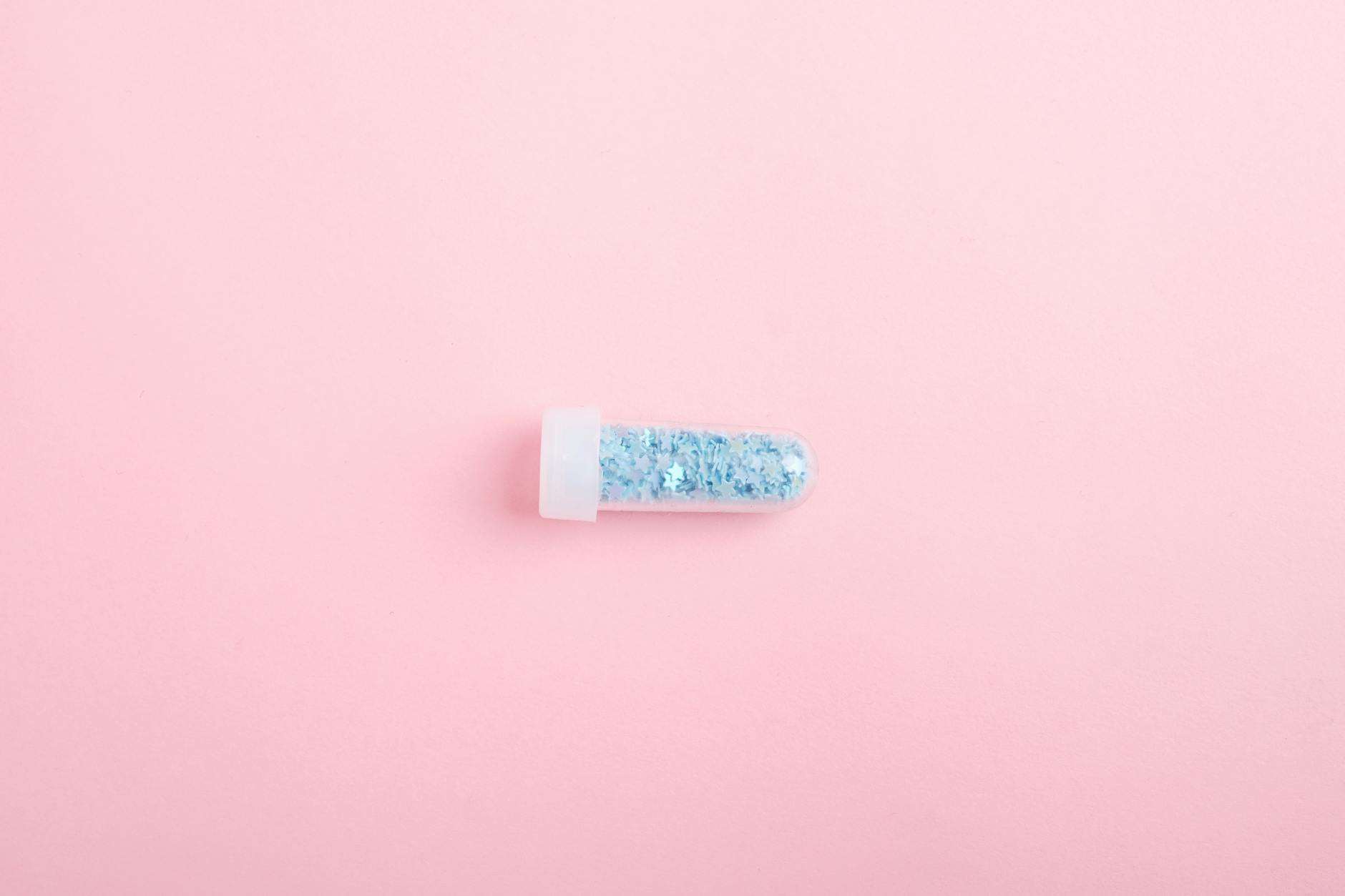 Top view of tube full of shimmering blue glitter for design and decoration on pink background