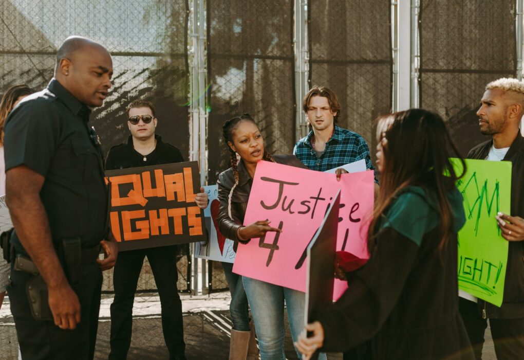 Poder Legislativo debate permanência de sessões híbridas Protesters holding signs demand justice and equal rights in street confrontation with a policeman.