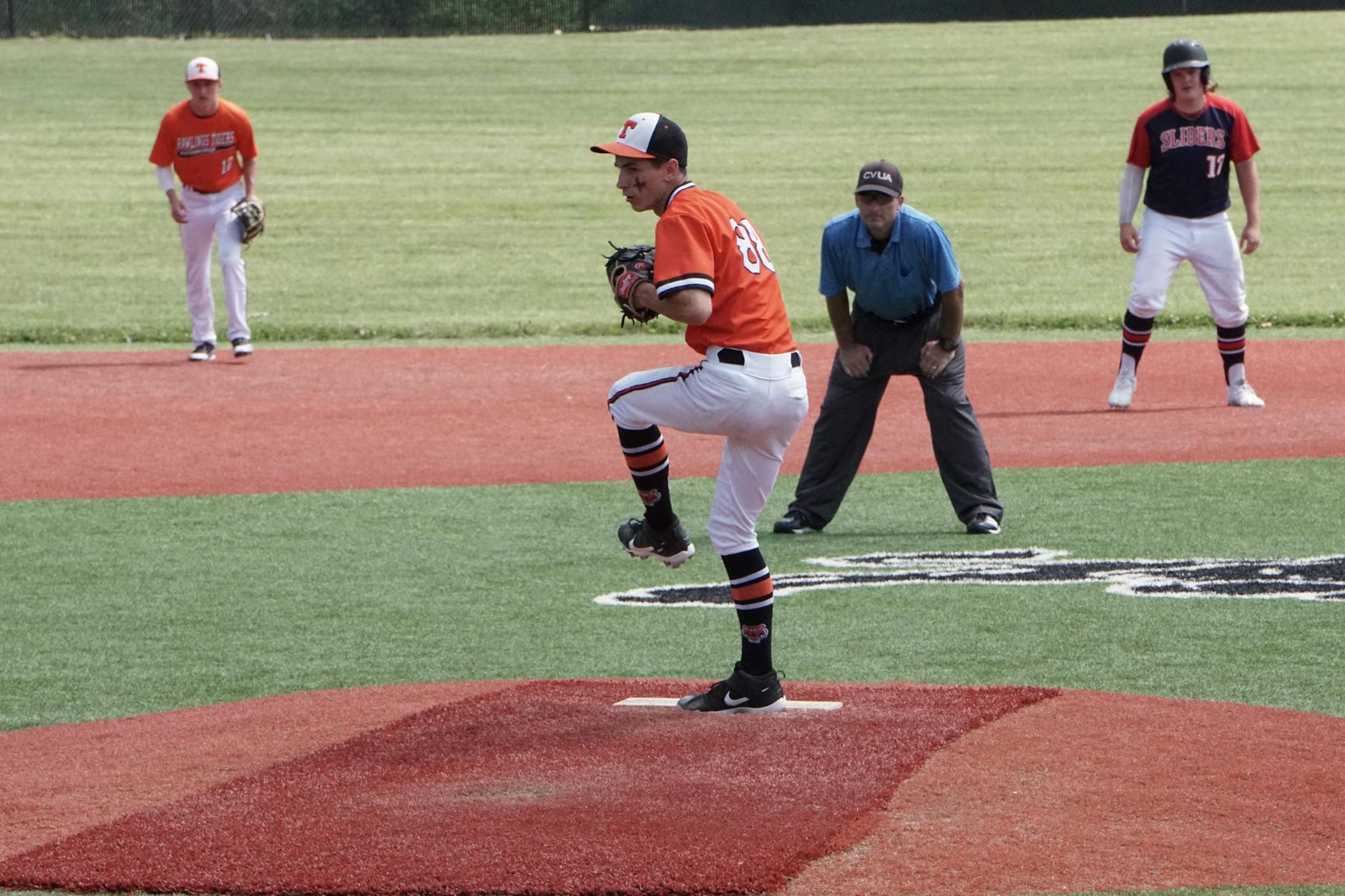 Action shot of a baseball pitcher winding up to throw a pitch on a sunny outdoor field.