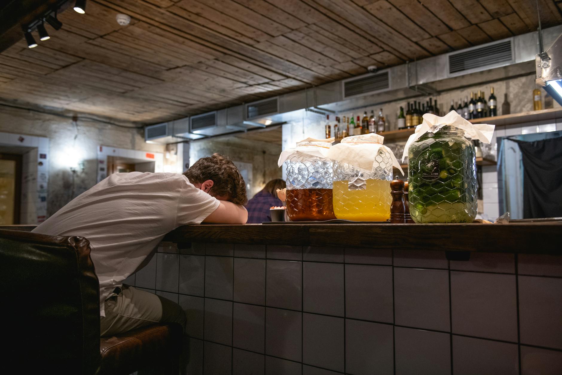 A man rests at a cozy bar counter in Moscow with jars and a rustic ambiance around him.
